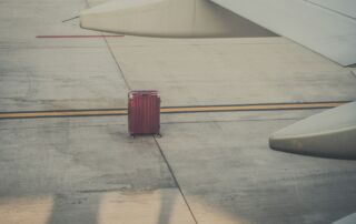 red hard shell lost luggage by an airplane wing