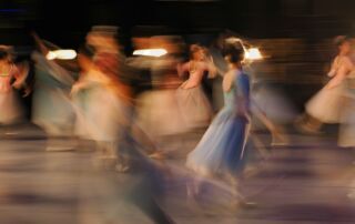 A group of dancers in long dresses moving across a stage in motion blur