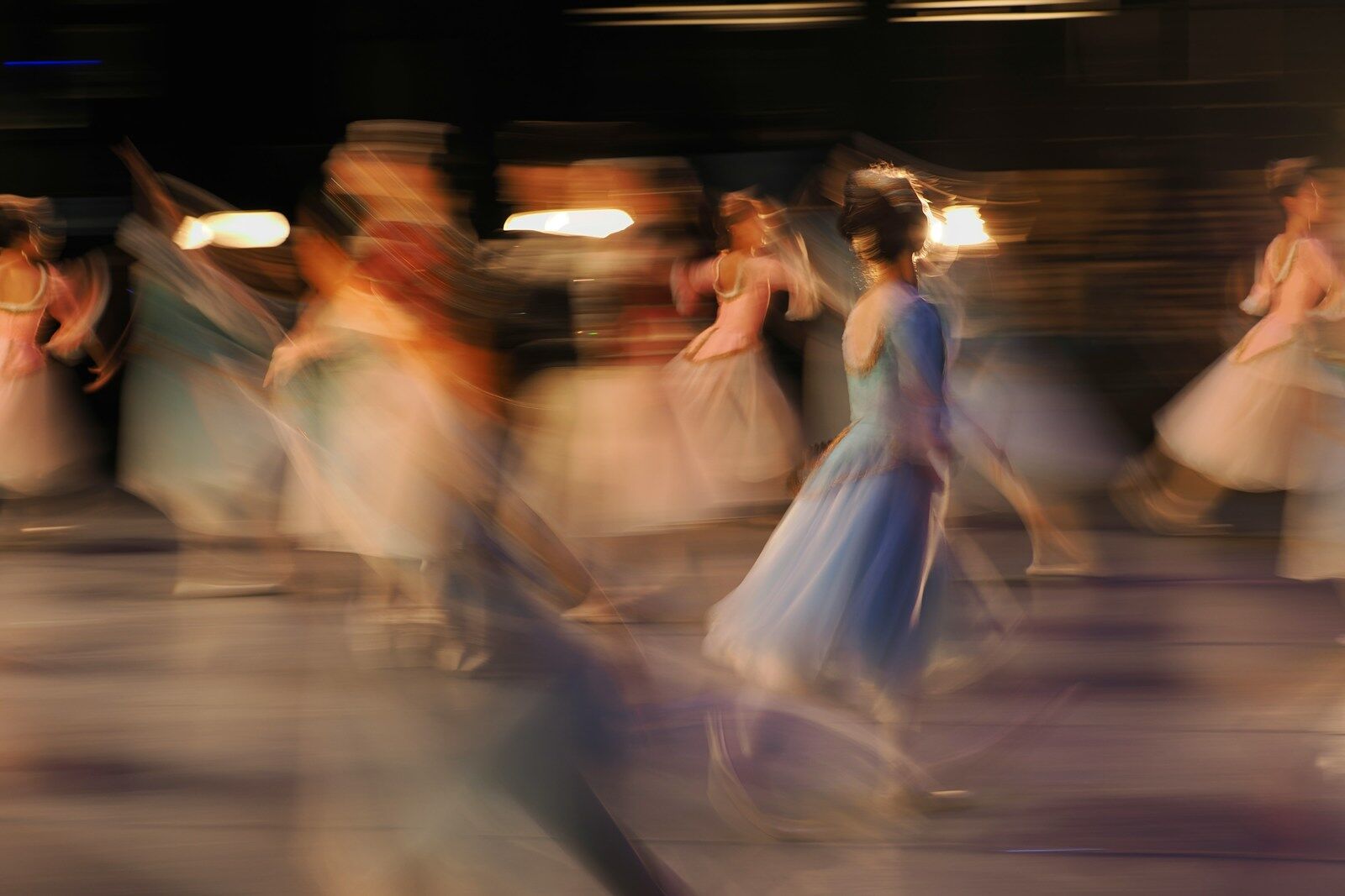 A group of dancers in long dresses moving across a stage in motion blur