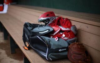 a baseball glove, catchers mitt, and helmet sit on a bench