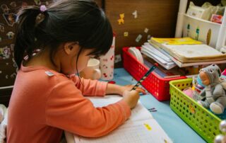 girl in pink long sleeve shirt writing on white paper