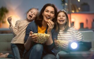A woman and two children eating popcorn while watching a movie at home