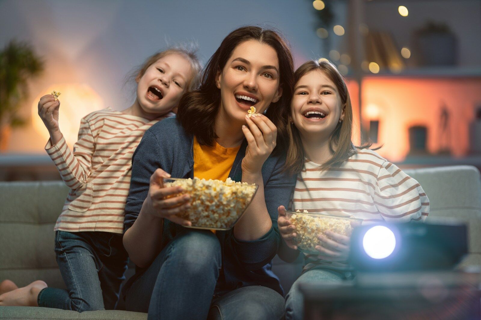 A woman and two children eating popcorn while watching a movie at home